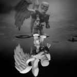 A lego skeleton with wings stands in a puddle and his ghastly reflection stares back out to the viewer in this black and white outdoor toy photograph.