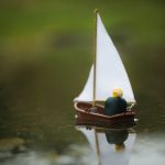 Lego Legolas sits in the back of a lego sailboat and sails away in a small puddle to parts unknown.