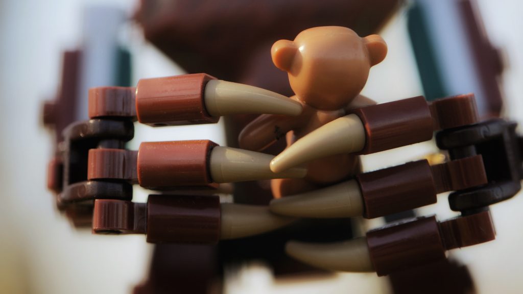 The large lego hands of Groot cradle a small lego teddy bear in this close up image.