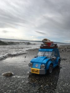 A Blue LEGO Volkswagen Bug sits next to the surf. A grey and threatening sky looms overhead.