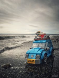 A Blue LEGO Volkswagen Bug sits next to the surf. A grey and threatening sky looms overhead.