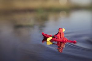 red classic lego spaceman kayaks across the still pond taken with a lensbaby by shelly corbett