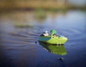 Lego Swamp Monster drives a green power boat across the blue lake by Shelly Corbett