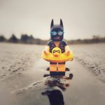 lego batman, dressed in swim wear, stands in a puddle looking for the beach