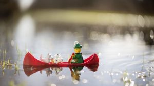 Classic LEGO woodsman mini figure paddles a red canoe with a white scotty dog and white flowers in his boat.