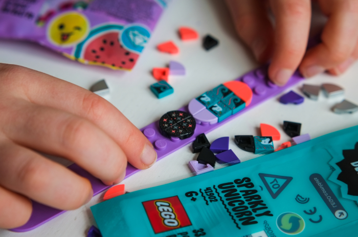 child's hands are building the bracelet from Lego bricks and tiles