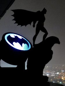 Rooftop silhouette of Batman action figure with bat signal