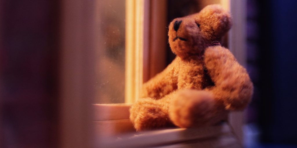 A small brown plush teddy bear sits in the window waiting to be seen by the passing children. Image by Janan Lee