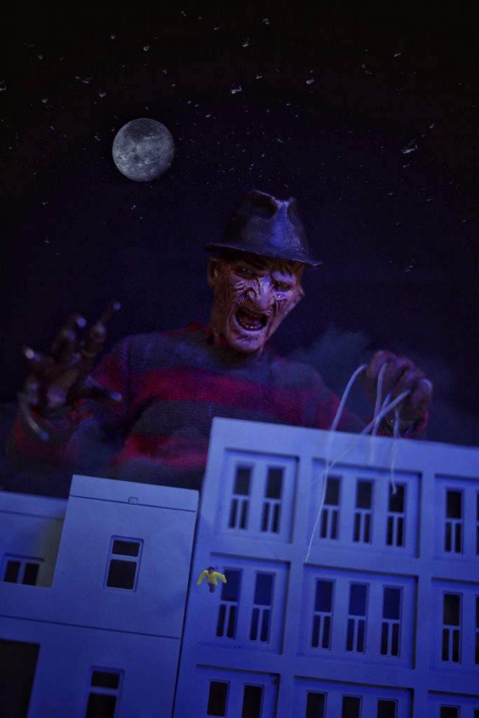 Giant 1:6 scale Freddy Krueger action figure laughing over buildings as person falls by @tromatic_exposure