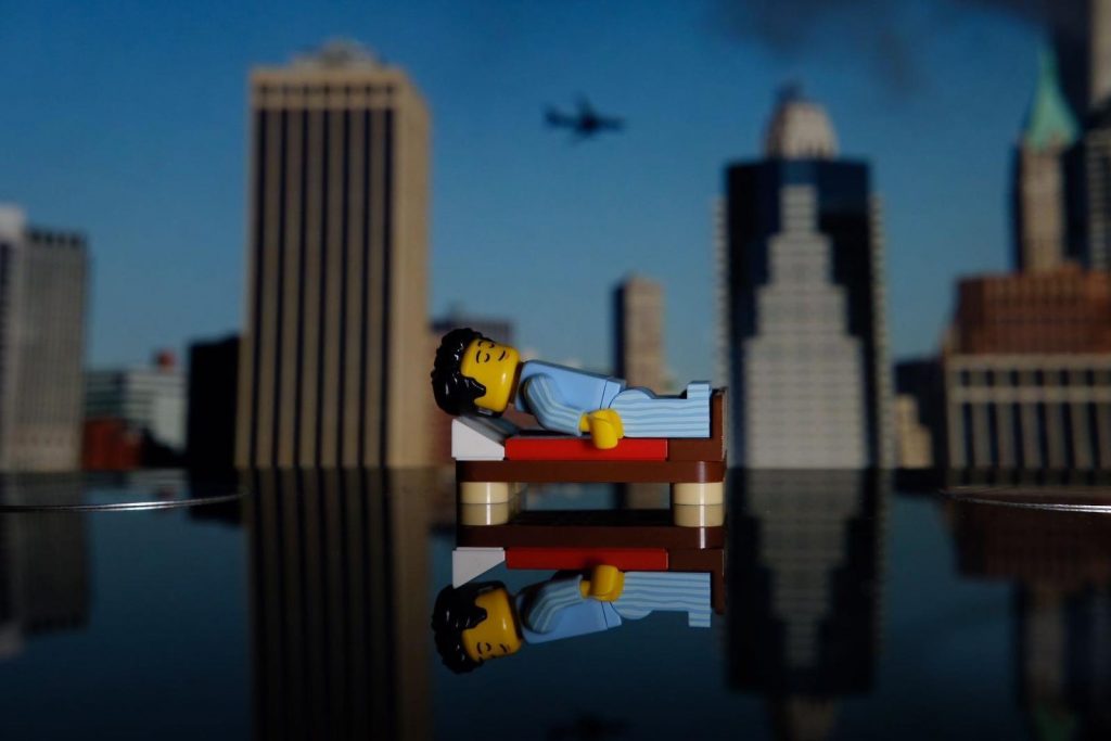 Lego minifigure lying on bricks-made bed with New Yor skyline in the background