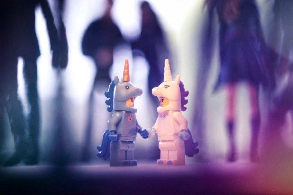 Two Lego unicorn minifigures looking at each other among the crowd of larger action figures