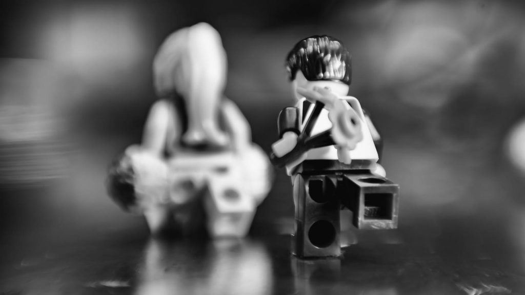 Two Lego minifigures shot from behind. Minifigure in the foreground is holding flowers and is chasing the second minifigure