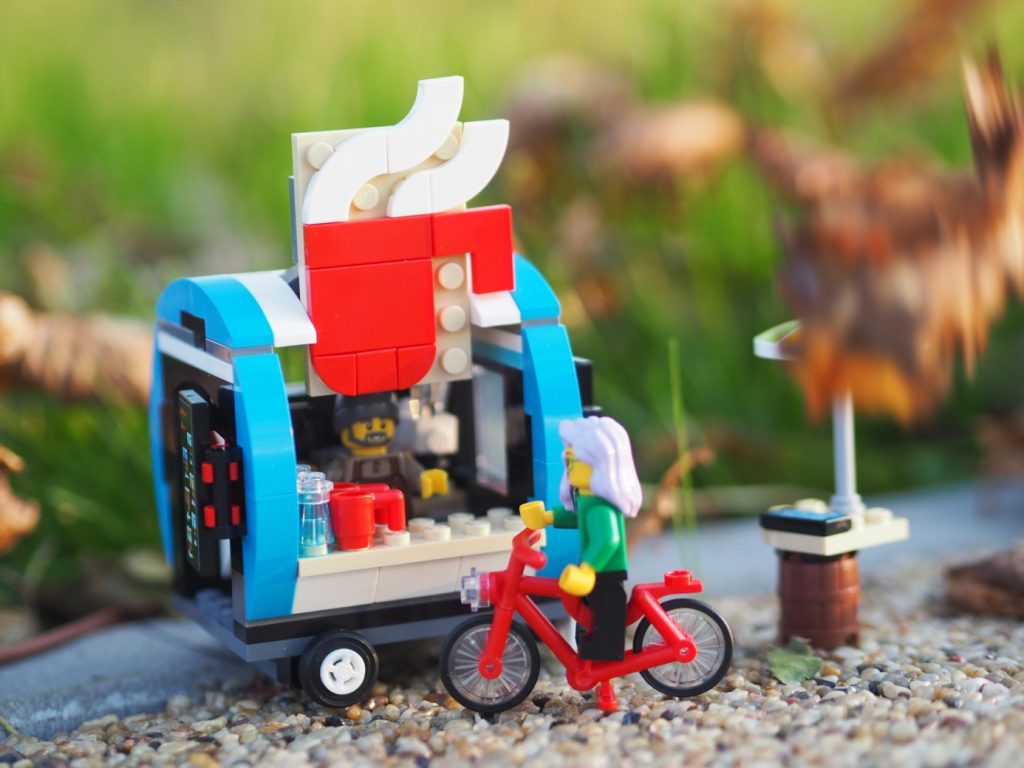 A LEGO female minifigure on the red LEGO bike approaching LEGO coffee cart.