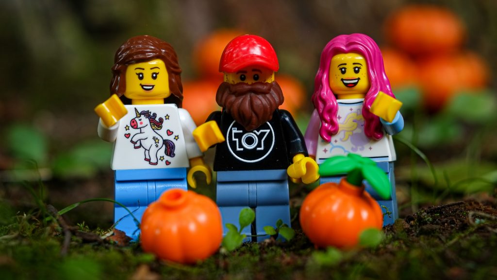 Three LEGO minifigures, two female and one male, waving hands and standing on the LEGO pumpkin field.