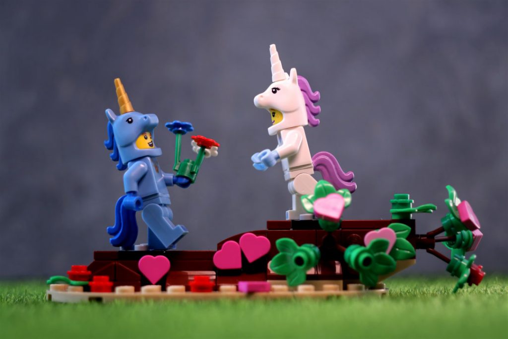 A unicorn suit guy minifigure giving a flowers to unicorn girl minifigure standing on stand from LEGO 40522 lovebirds set