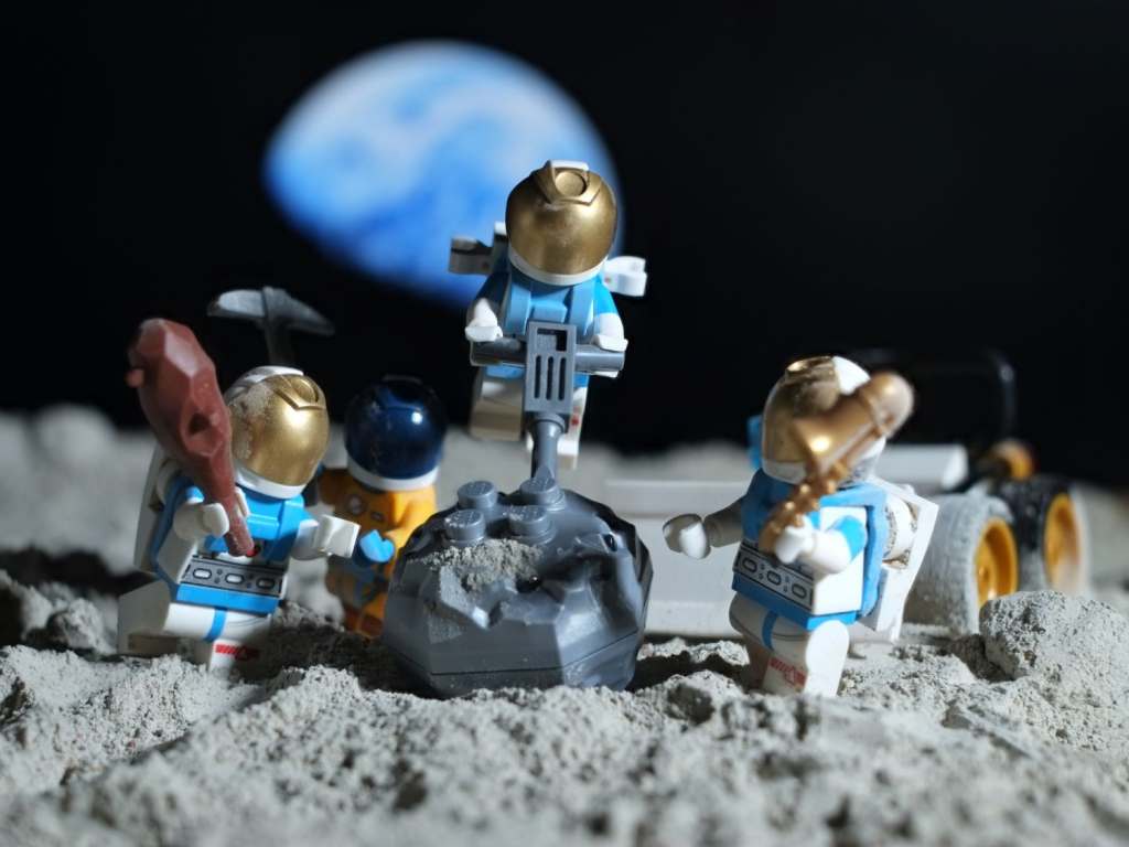 a group of LEGO astronauts trying to break a stone on the Moon surface