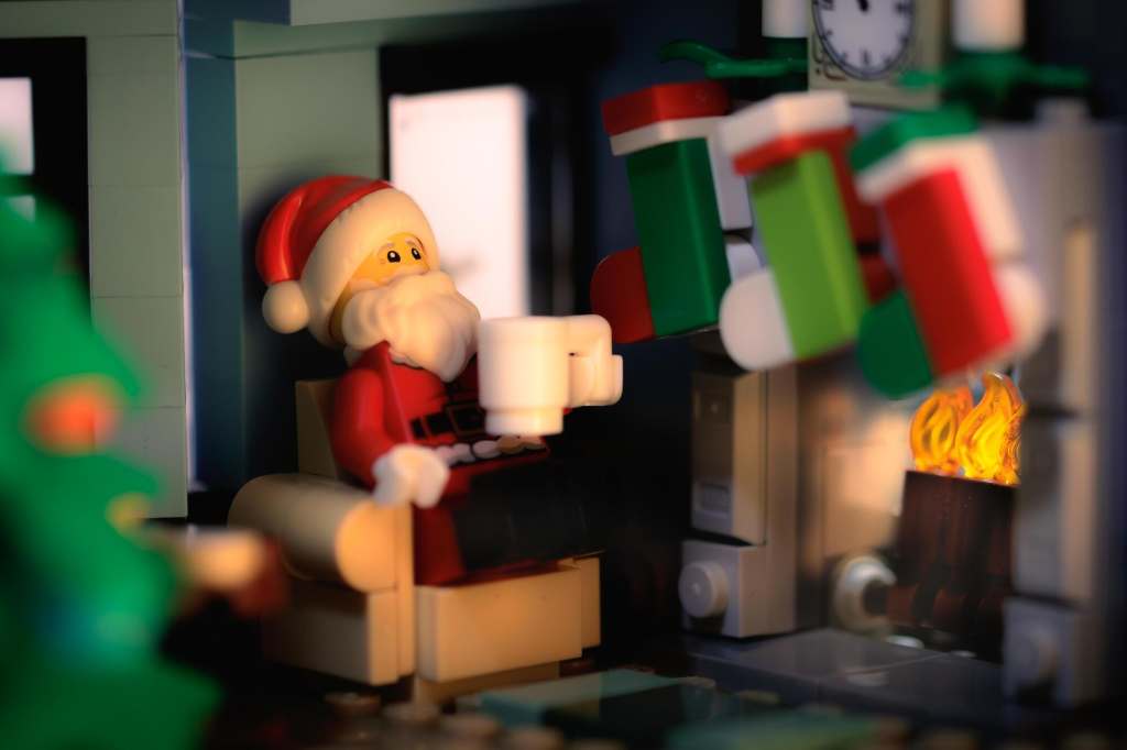 a Lego Santa Claus minifigure sitting by the fireplace with cup in hand