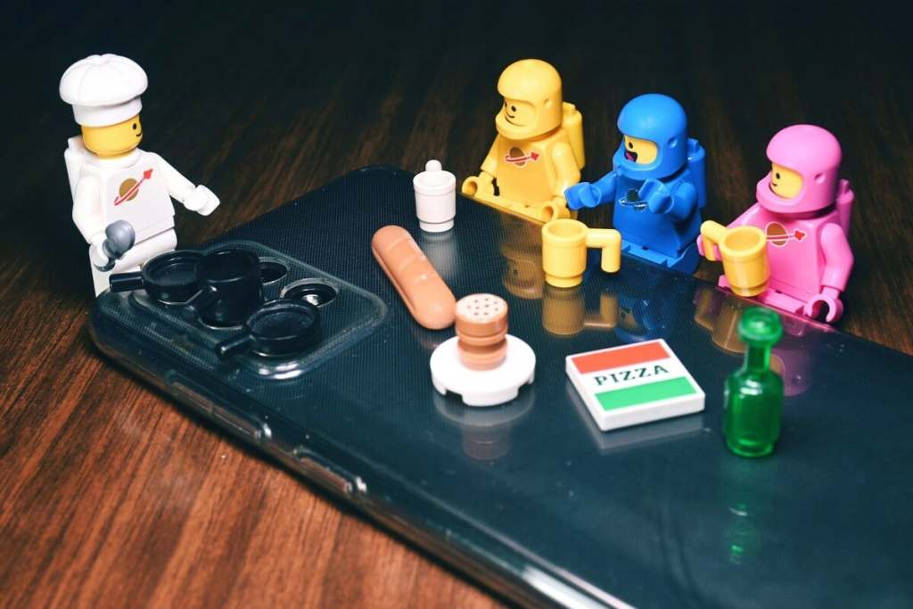 LEGO minifigures partying on the back of the smartphone with phone's camera lens as stove burner