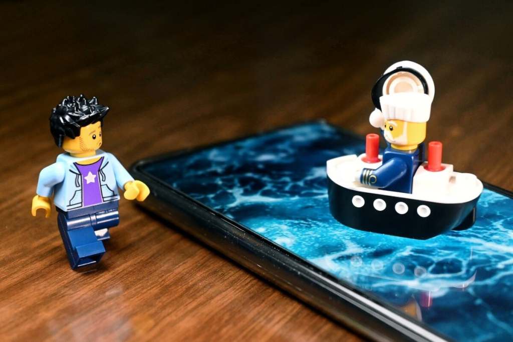 LEGO ship captain minifigure sitting in a little ship, put on the smartphone screen with sea surface display