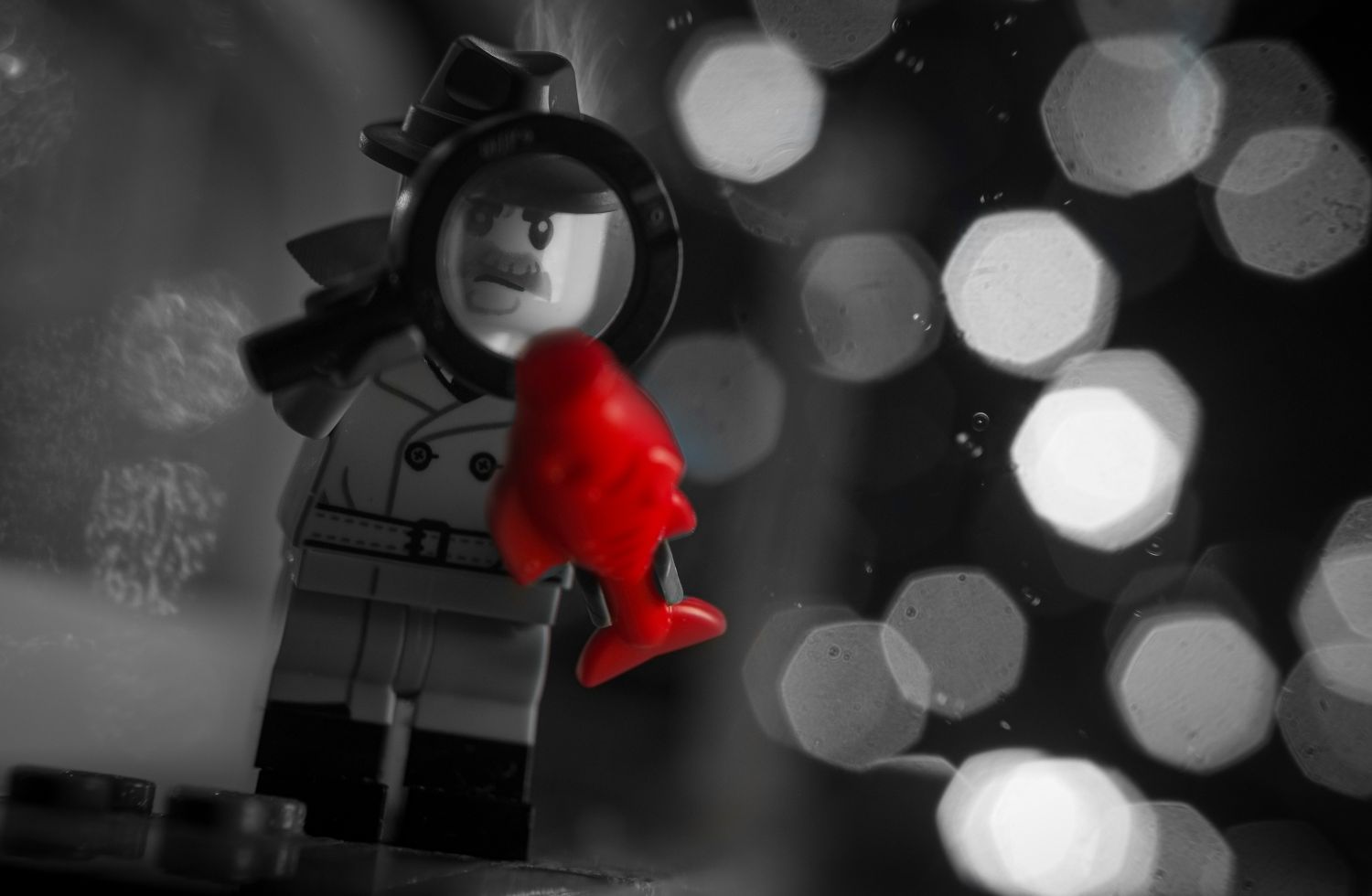 A LEGO noir detective in black and white, holding a red LEGO herring piece.