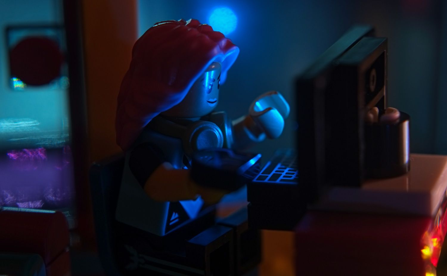A LEGO video player minifigure in low key, lit only by the light form the computer monitor.