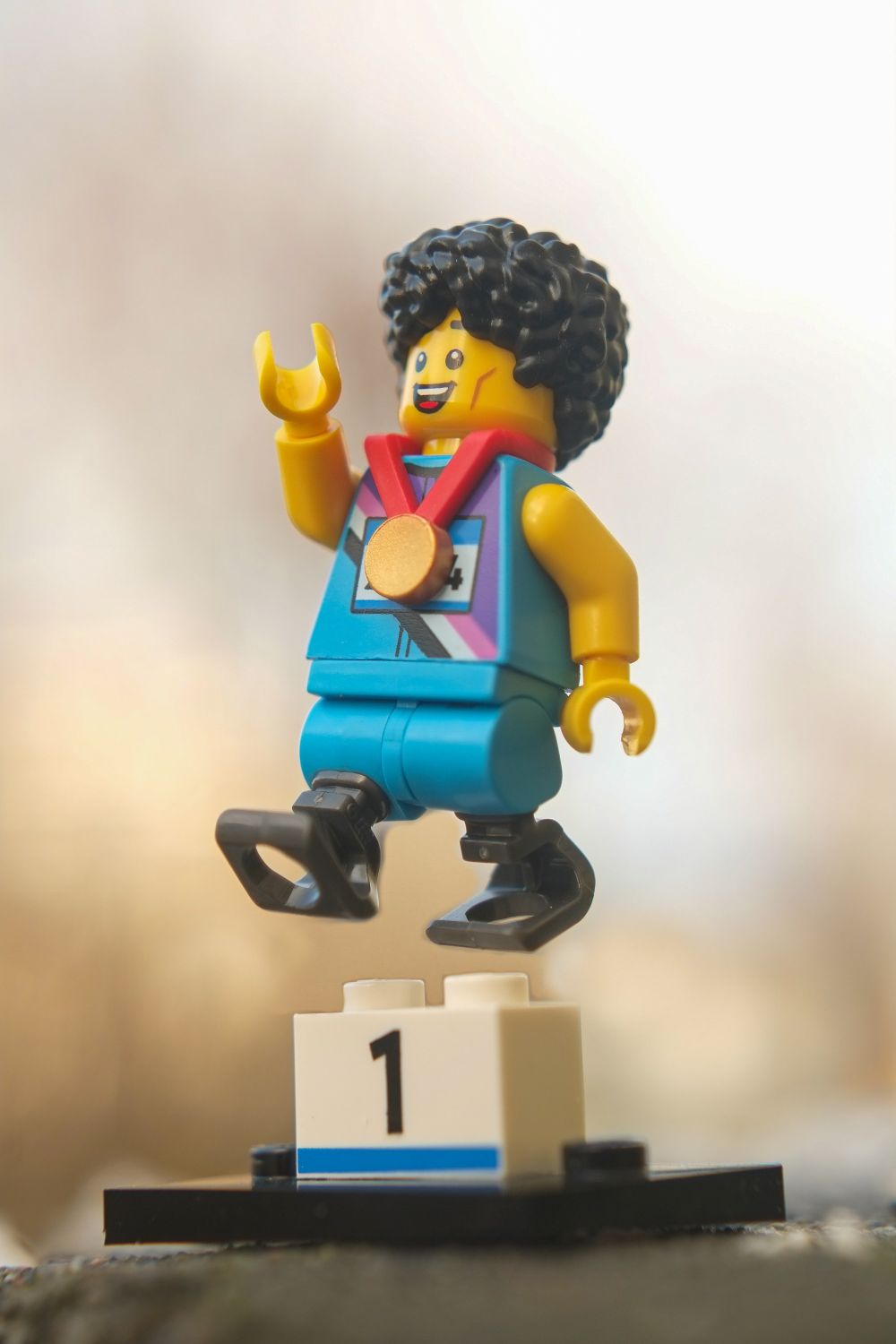 A LEGO paralympic athlete with prosthetic legs and medal on his neck is jumping over the podium.