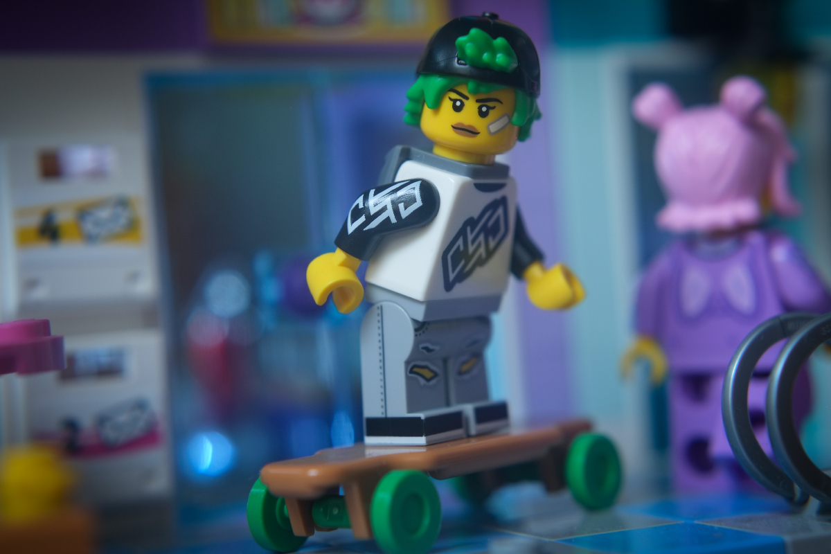 Longboarder minifigure with a concentrated face drives along the brick-built sidewalk on her longboard.