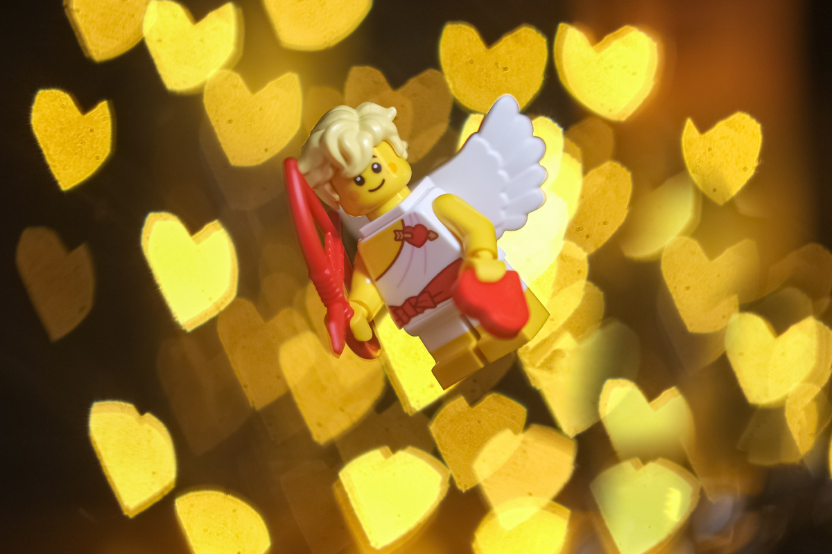 Smiling Cupid minifugure flies against the background of intense heart-shaped bokeh.